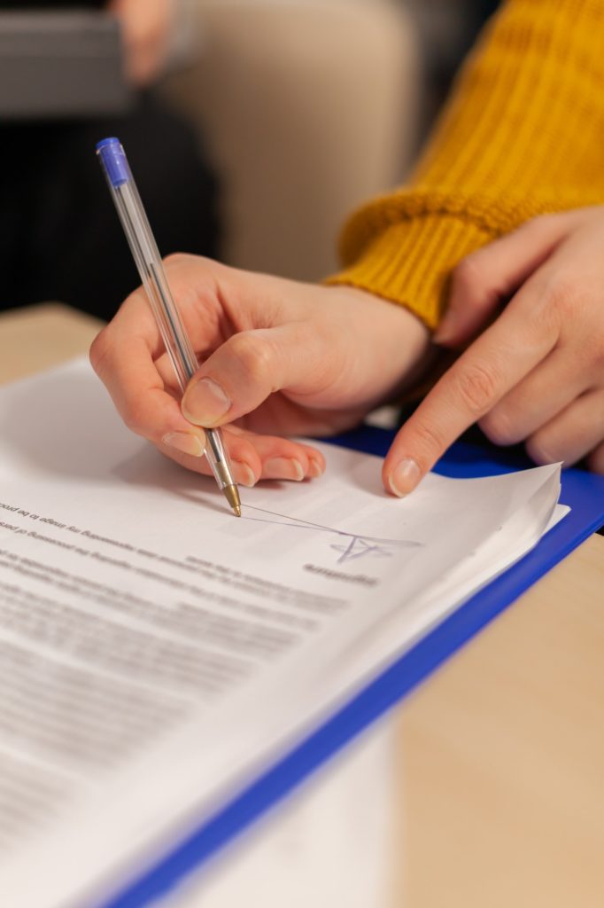 Businesswoman signing paper, partner hand puts signature on document